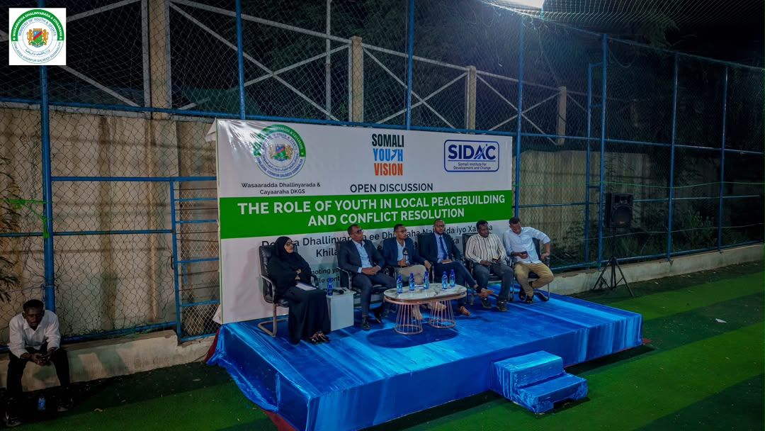 Panellists seated on a blue stage in front of the youth peacebuilding discussion banner